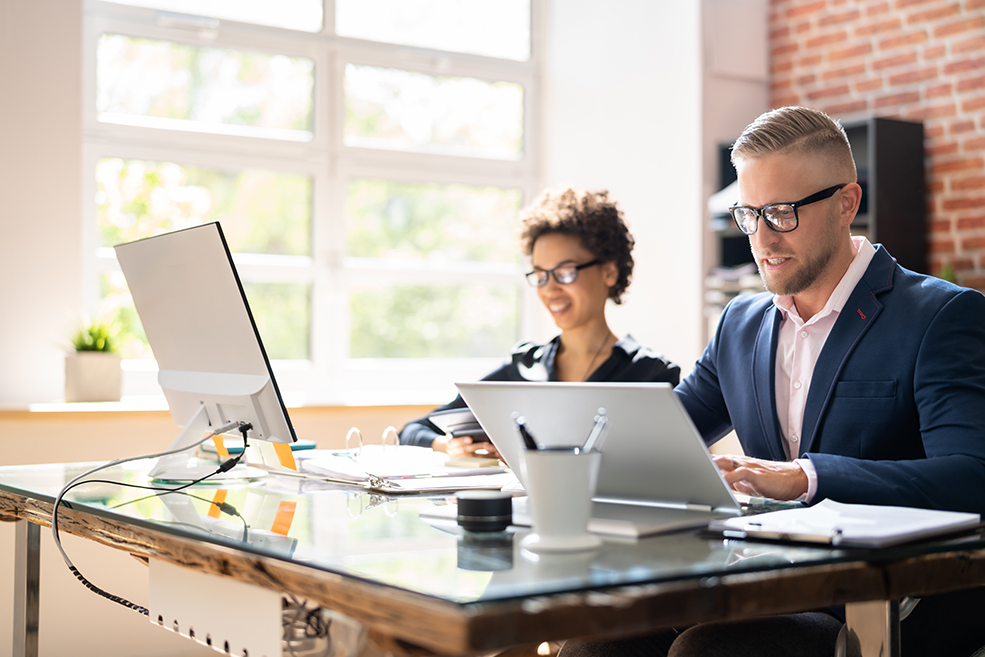 Business man and woman at a desk on their computers analyzing and forecasting data.