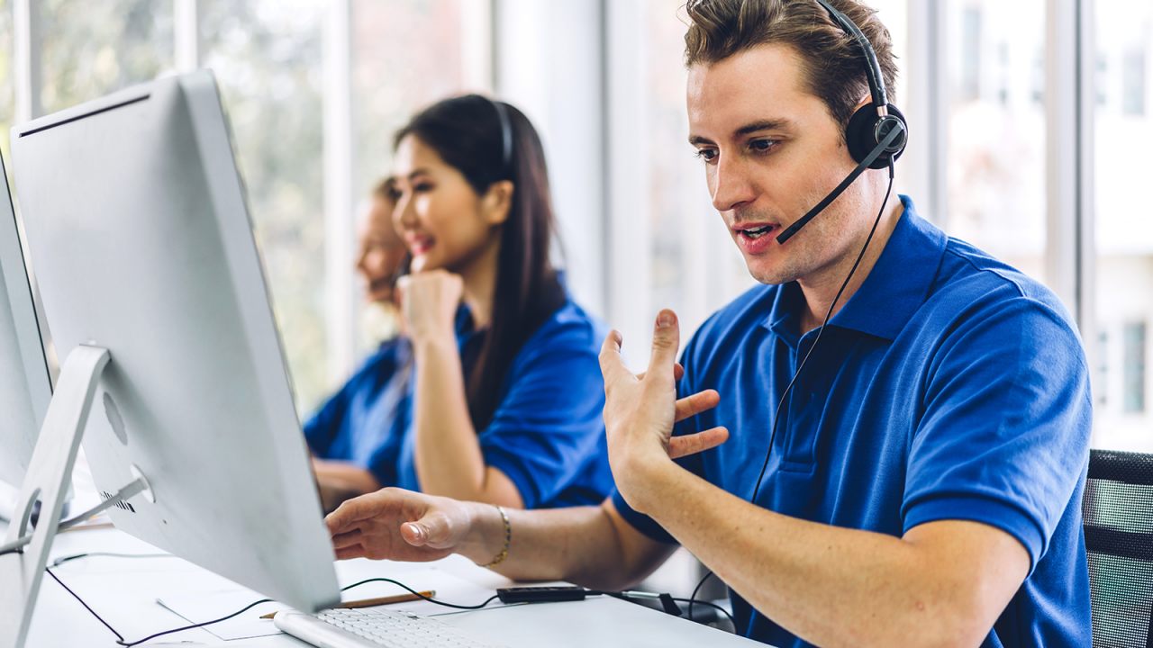 Group of happy call center agents working and talking with headset on desktop computer at call center.